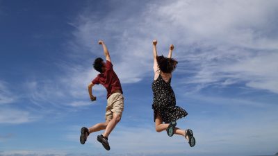 Två personer som hoppar framför en blå himmel med moln på.